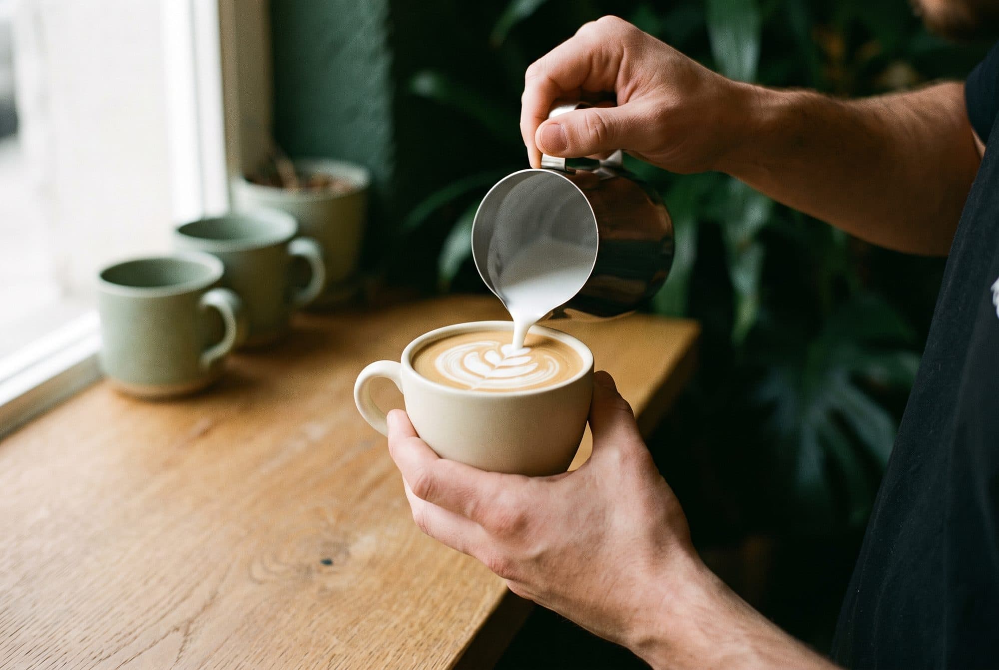 Manos de barista dibujando latte art con la jarra de leche